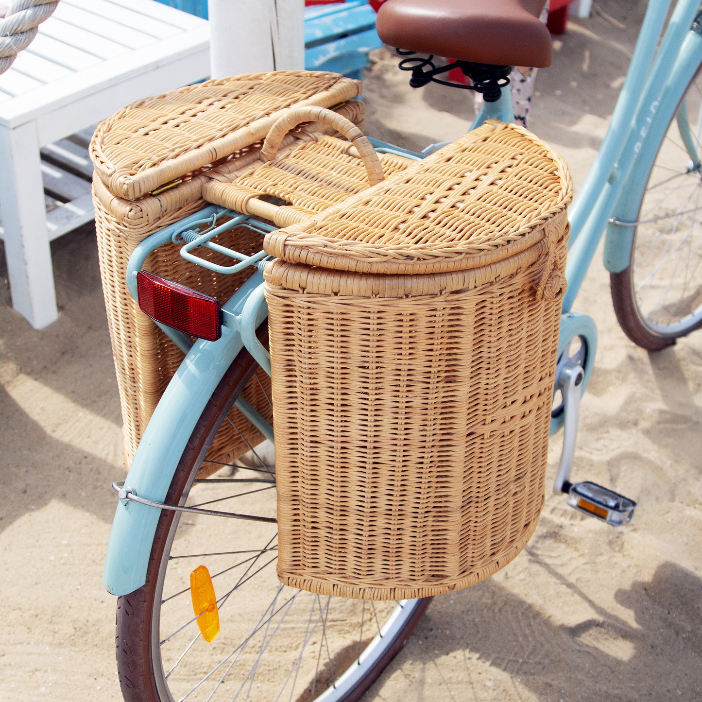 Handwoven bike basket on the back of a blue bike on sand at the beach