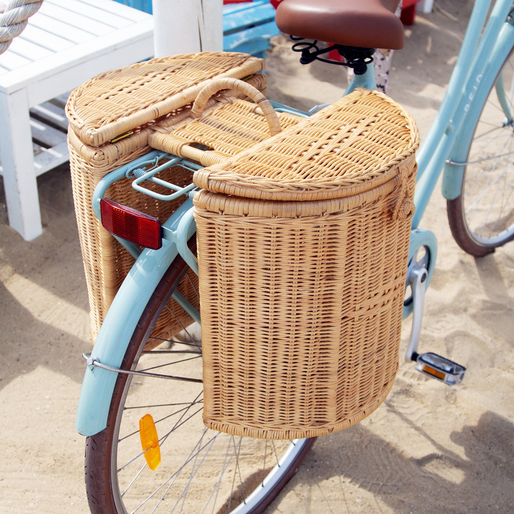 Handwoven bike basket on the back of a blue bike on sand at the beach